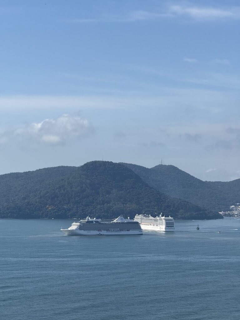 Two cruise ships anchored in the bay off Barra Sul, with a green hill behind