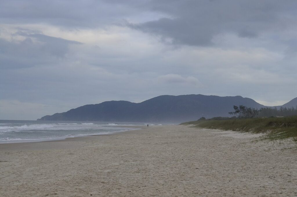 The long, open sand of Praia do Campeche on a grey day, hills in the distance
