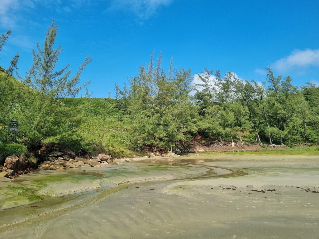 A small stream crossing the sand at Praia Vermelha, Garopaba, with green hillside behind